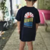 Enfant portant le T-shirt Gouyat ESTEY Enfant de dos en T-shirt coton bio « Gouyat » ESTEY bleu marine, imprimé soleil et vagues