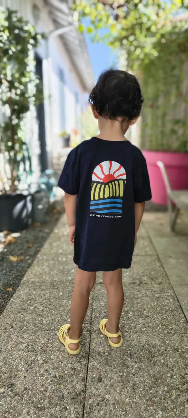 Enfant portant le T-shirt Gouyat ESTEY Enfant de dos en T-shirt coton bio « Gouyat » ESTEY bleu marine, imprimé soleil et vagues