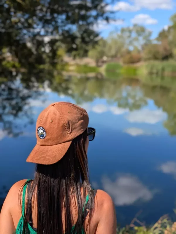Casquette Le Cap Estey camel portée de dos au bord de l’eau Casquette Le Cap Estey en velours côtelé camel portée de dos au bord d’un plan d’eau