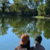 Casquettes Le Cap Estey portées au bord de l’eau Deux personnes portant la casquette Le Cap Estey au bord d’un plan d’eau bordé d’arbres