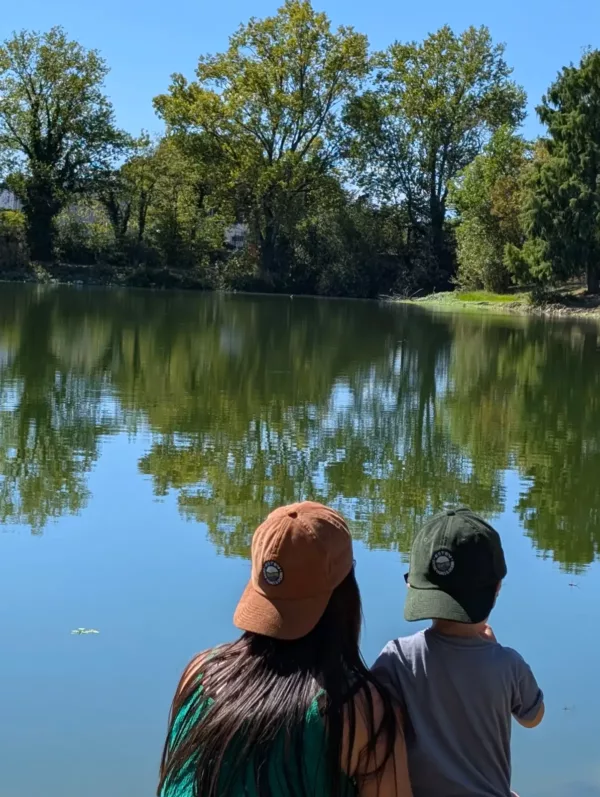 Casquettes Le Cap Estey portées au bord de l’eau Deux personnes portant la casquette Le Cap Estey au bord d’un plan d’eau bordé d’arbres